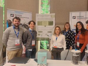 5 people gathered in a conference booth with a poster presenting the project. Gaiker and DTI representatives are present