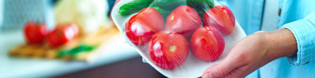 platter of tomatoes wrapped in plastic being held by someone, only one hand shows